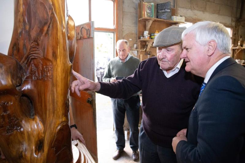 The late Phil Bourke explaining one of  his many wood carved pieces to former GAA President Aogán O'Fearghail at his workshop in Upperchurch